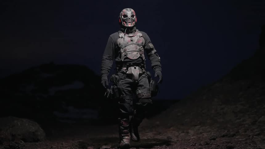 Person wearing a mask and costume walking through a natural environment illuminated by a light