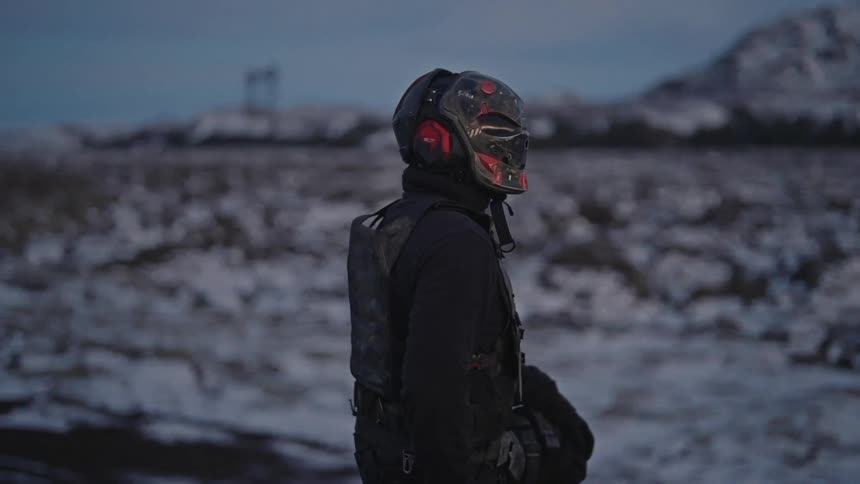 Shadowy person wears a distinctive helmet with red and black accents positioned against a winter backdrop