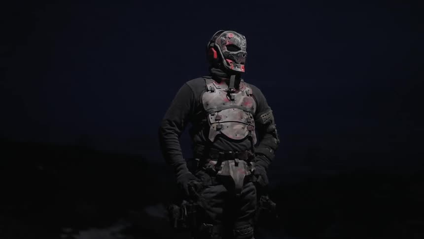 A masked figure wearing a dark tactical outfit with a weathered almost postapocalyptic look