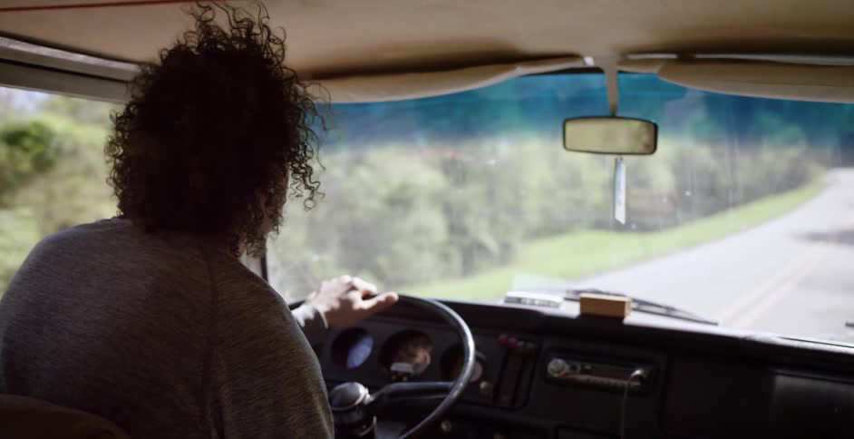 A person with curly hair is driving down a road