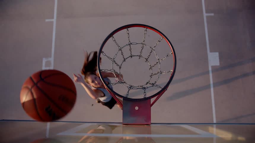 A woman throwing an orange basketball into a hoop with a red rim and metal chains