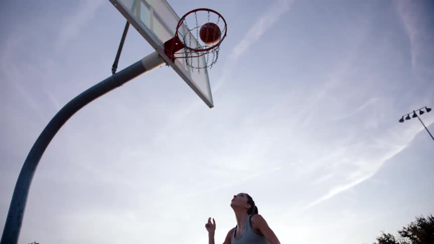 Woman jumping and throwing a ball into the basketball hoop on a court