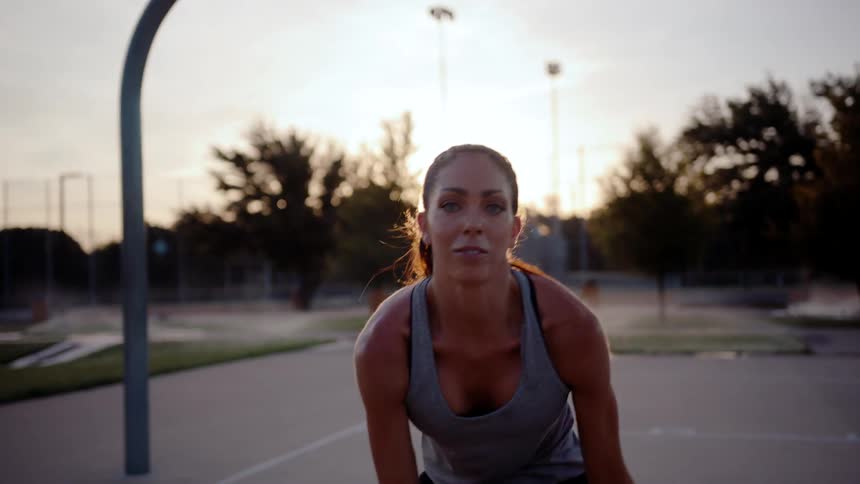 A woman showcases her basketball skills dribbling and performing tricks on a sunlit park court at dusk
