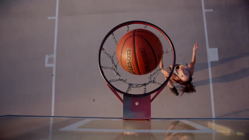 Woman jumping and hitting the ball into the basketball hoop on the court