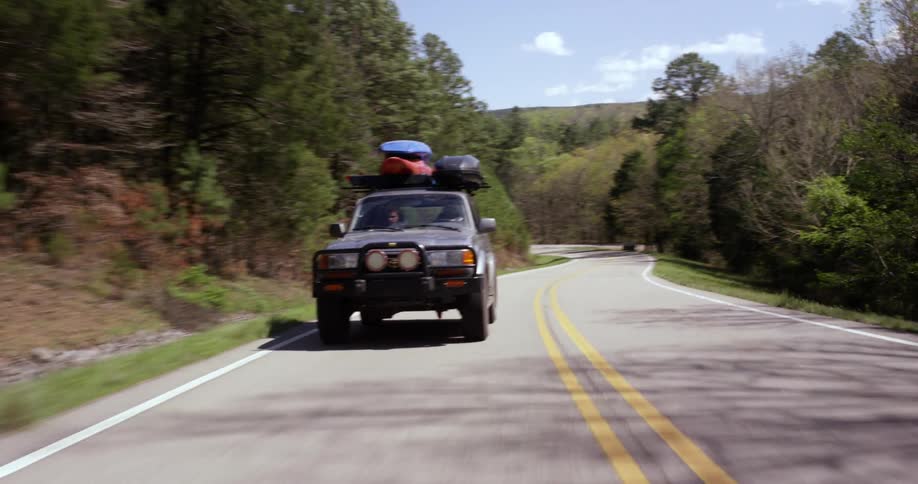 A vehicle rides through a forest with kayaks strapped to the roof
