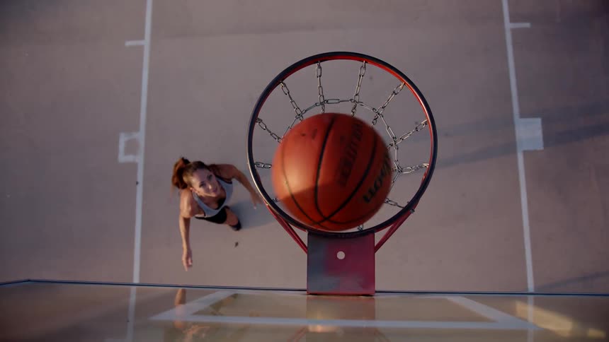 A woman throwing an orange basketball into a hoop with chains