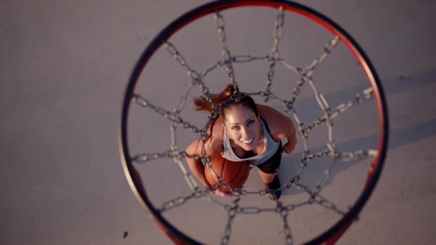 A woman walks under the basketball hoop while smiling
