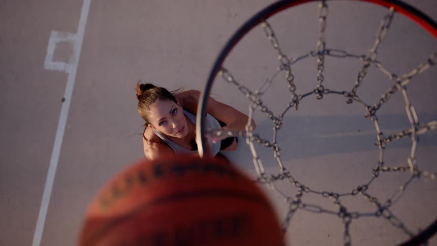 A woman highlighting an orange basketball in a basketball hoop with a chain net