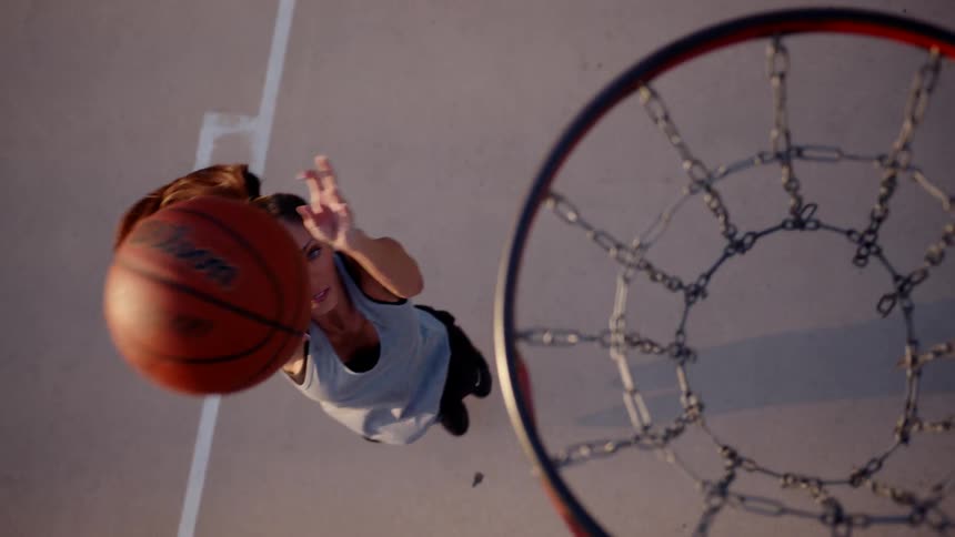 Top view of a woman jumping and hitting the ball into the basketball hoop on the court