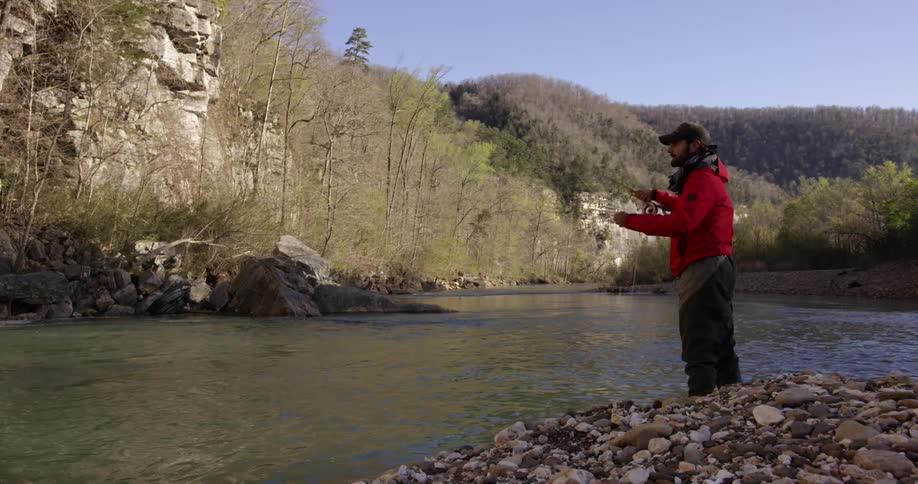 Bearded man in a red jacket fly fishing from the shore on a clear day