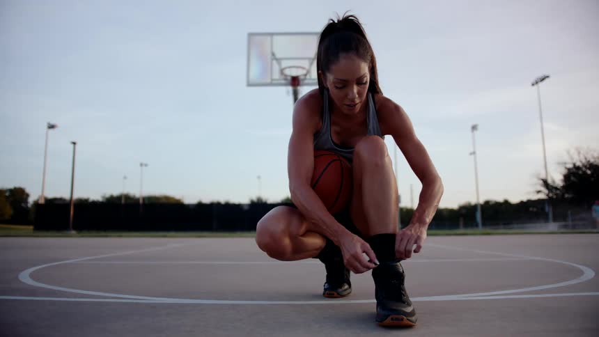 A woman is tying her sneakers on the basketball court