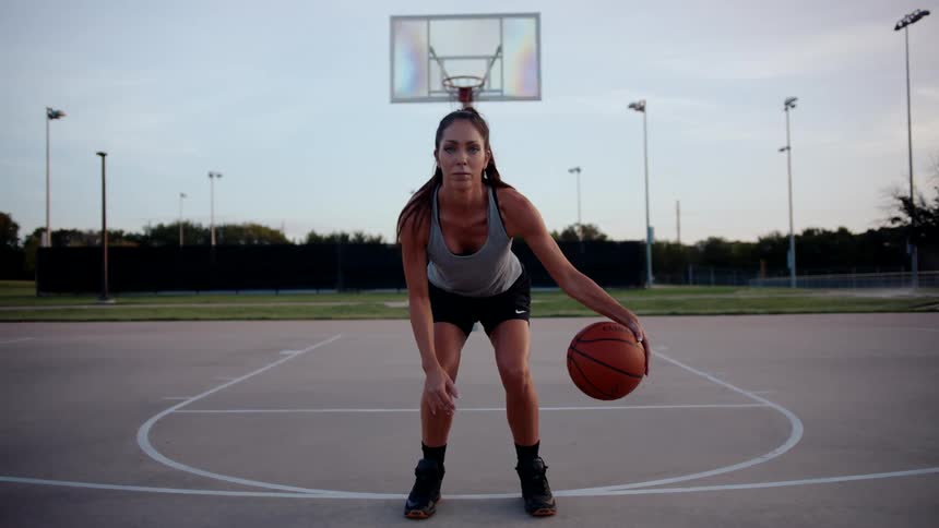 A woman is dribbling the ball on the basketball court