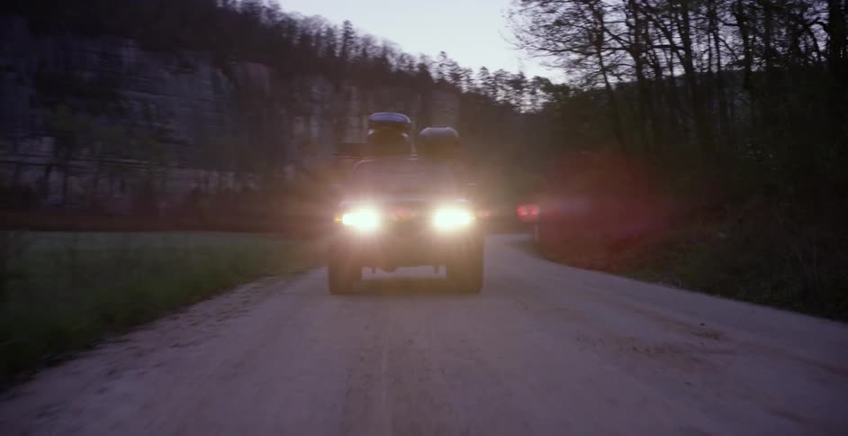 A car drives with its headlights on in the wilderness