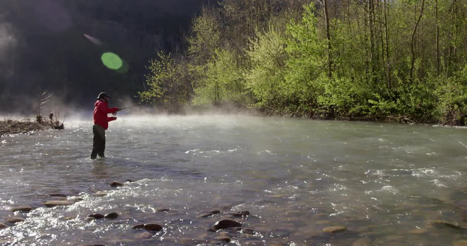 A fisherman stands in a river and casts a fishing line