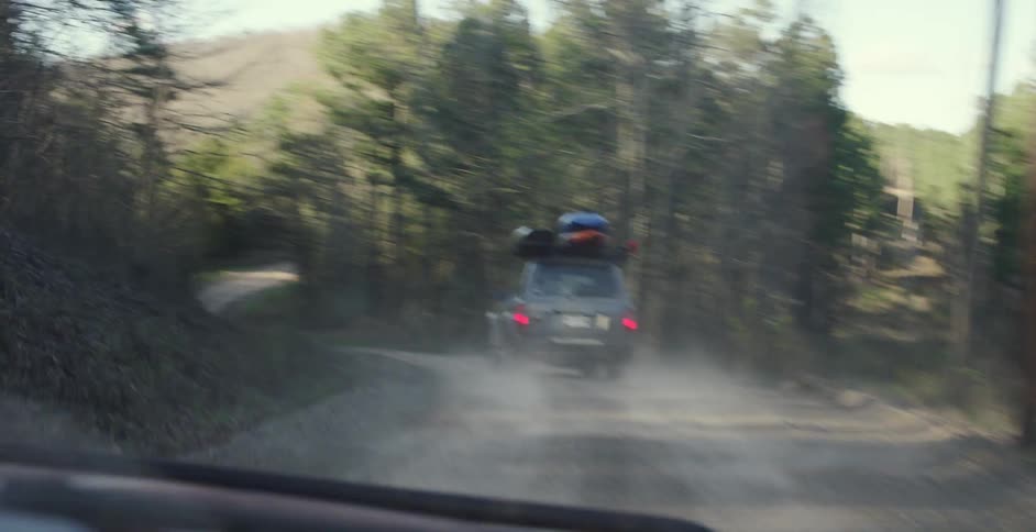 A vehicle drives through a forest with kayaks strapped to the roof
