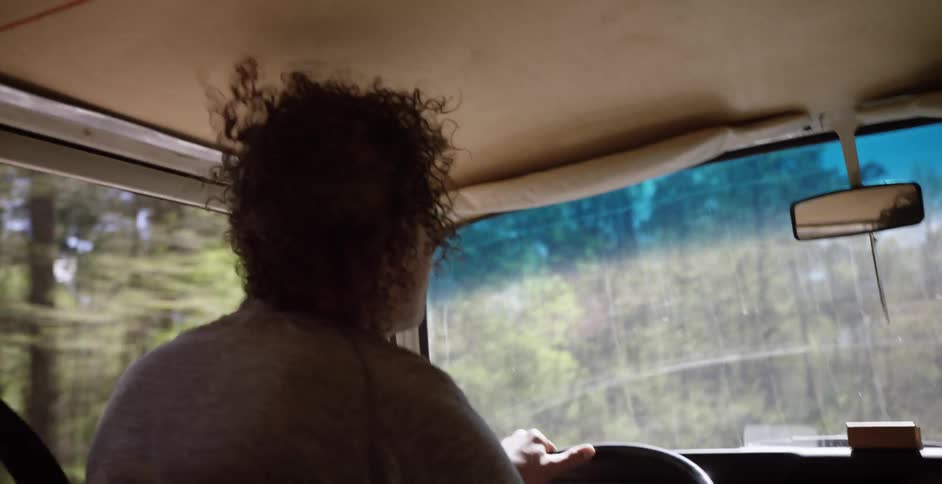 A man drives through a forested area with the window down