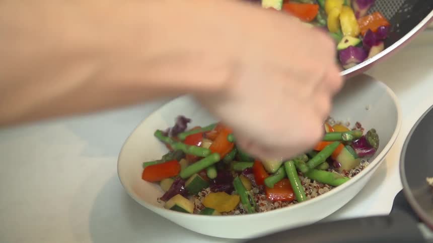 Someone spoons vegetables over a bowl of grains