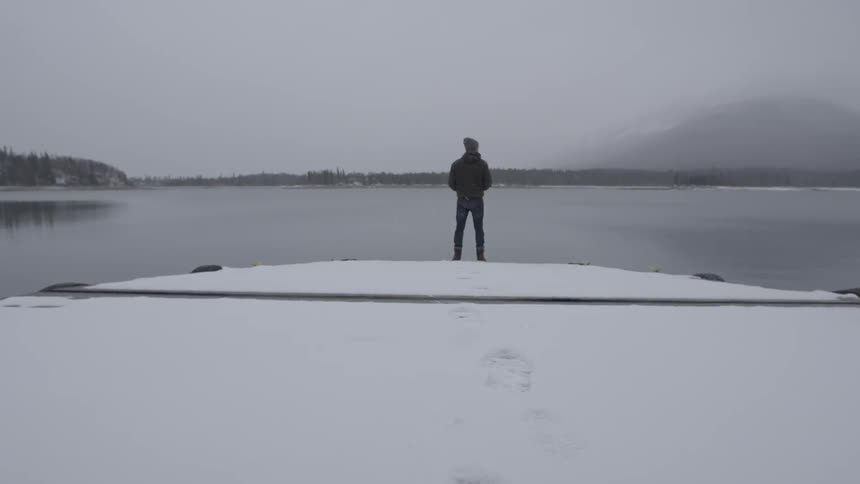 Man standing at the edge of a snowy piece of land overlooking the water
