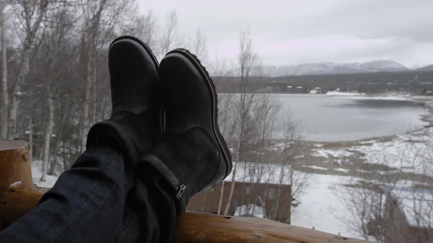 Person resting  their legs on a porch railing as they look upon a snowy wonderland