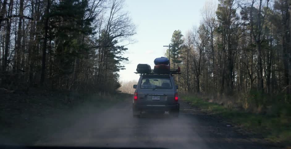 A truck carrying kayaks on top drives down a dirt road