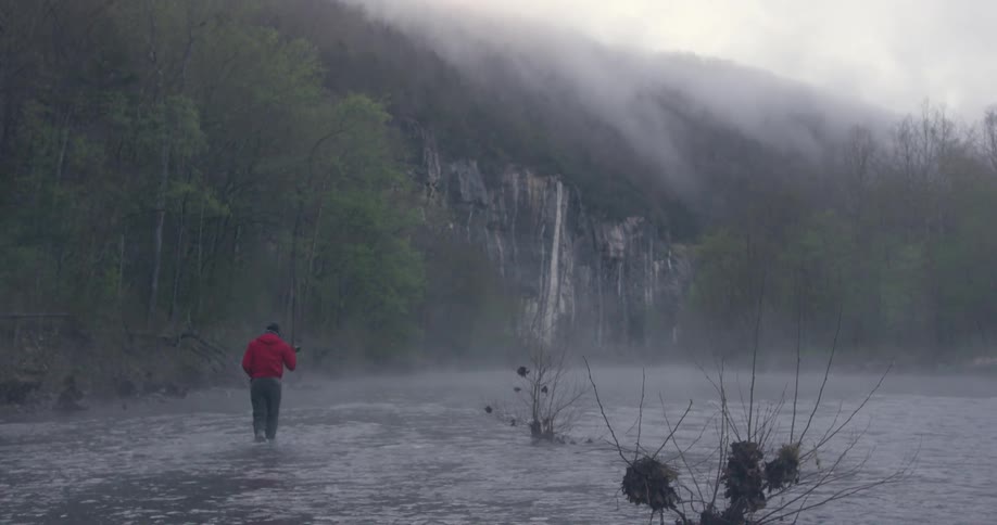 A man wades into a river in the fog