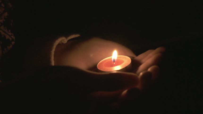 Someone holding a tea candle in the palm of their hands at night