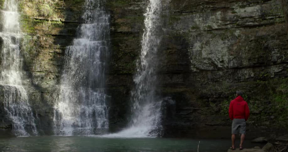 A person stands on the rocks below watching the waterfall