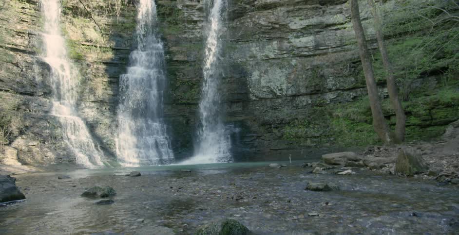 A man hops across rocks at the base of a waterfall