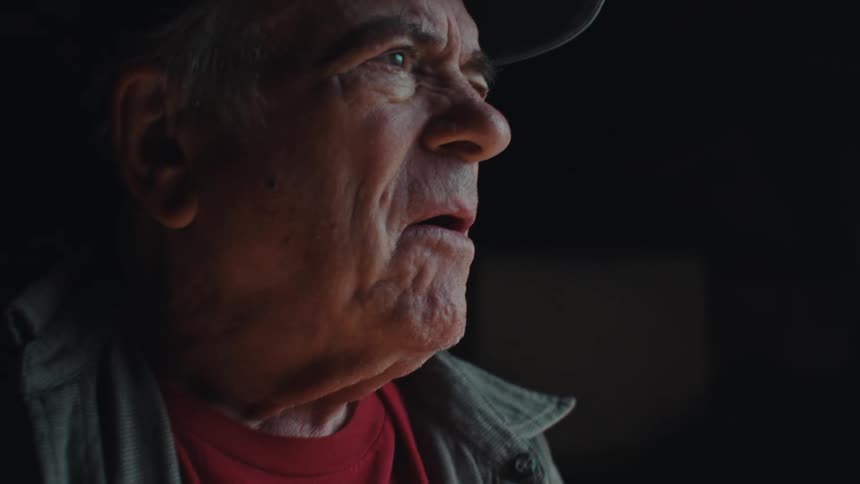 Elderly man smiles while sawing a narrow piece of wood in a shed