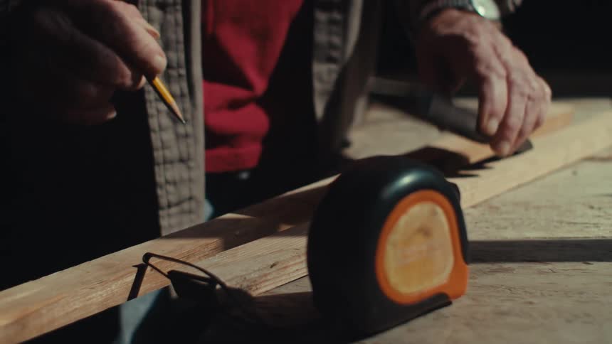 A man is marking measurements on a piece of wood
