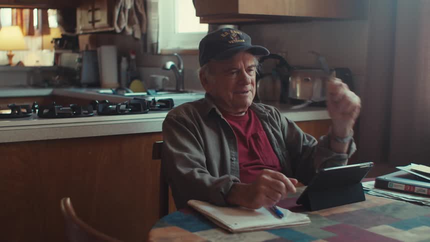 A man smiles and waves at his tablet