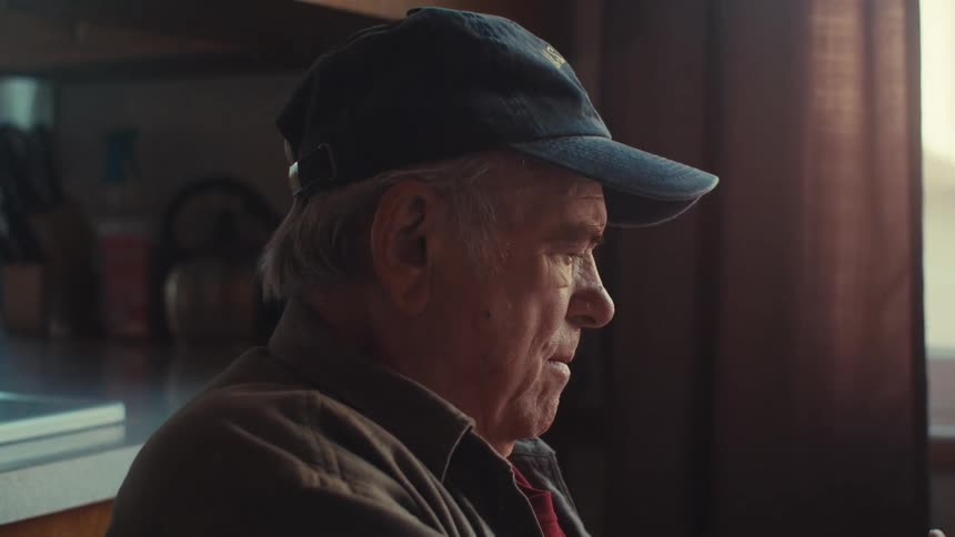 Elderly man in cap sitting interacting with a smartphone