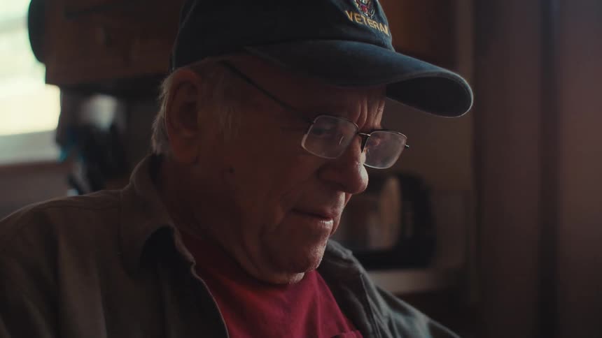 An elderly man writes in a paper notebook while scrolling on an electronic tablet