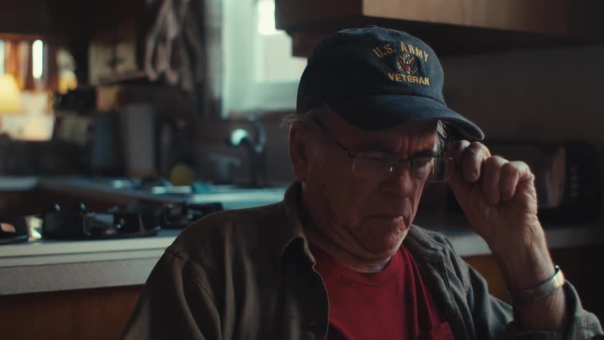 Elderly man sitting at table taking off his glasses