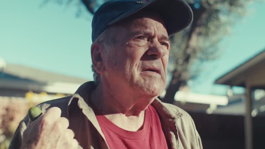 Elderly man in cap holding a wooden handle while standing in a backyard