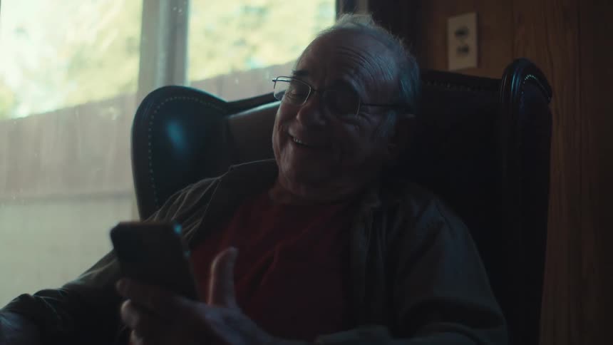 Elderly man sitting at home laughs during a video call on his smartphone