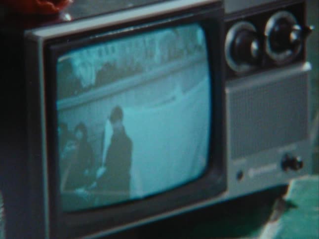 Woman standing in the kitchen watching an old television