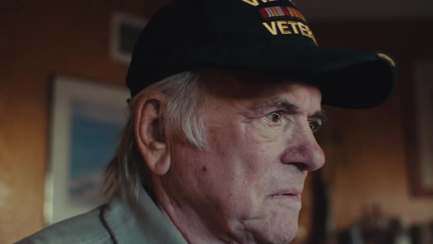 An old vietnam war veteran in a living room smiles and then suddenly becomes concerned