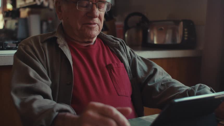 Elderly army veteran gestures while on a video call on a tablet on his kitchen table