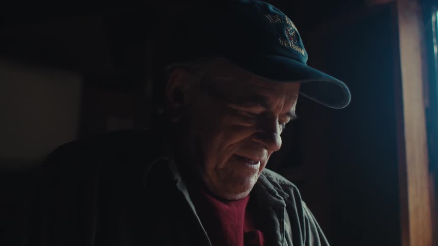 A man smiles and talks while looking down in the dark room