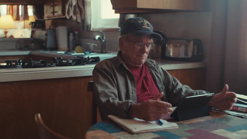 Elderly man sitting in front of a tablet and talking
