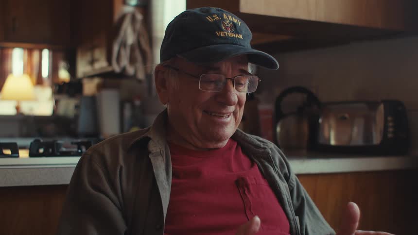 A man smiles and waves as he talks