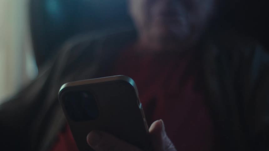 A mans hands hold a phone then the shot zooms out to reveal him smiling while looking at his phone