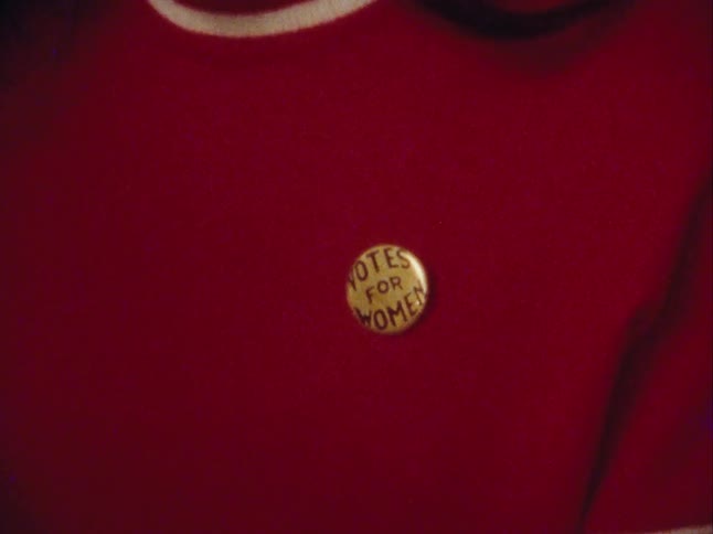 Woman wears a pin with the slogan votes for women