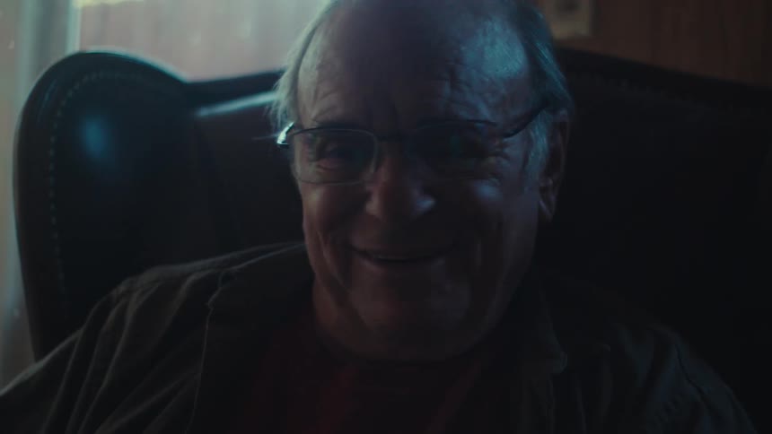 A close up of a smiling senior man seated in a chair talking to someone while gesturing and smiling
