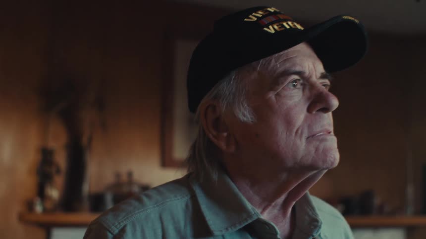 A man seemingly a veteran is shown holding an american flag and looking thoughtfully his expression serious