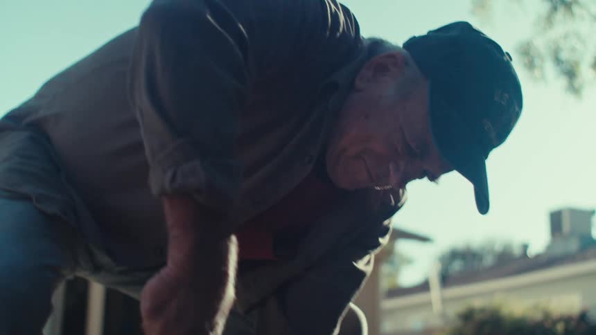 Elderly man in the garden of a backyard of a house cleaning dry fallen leaves from the grass