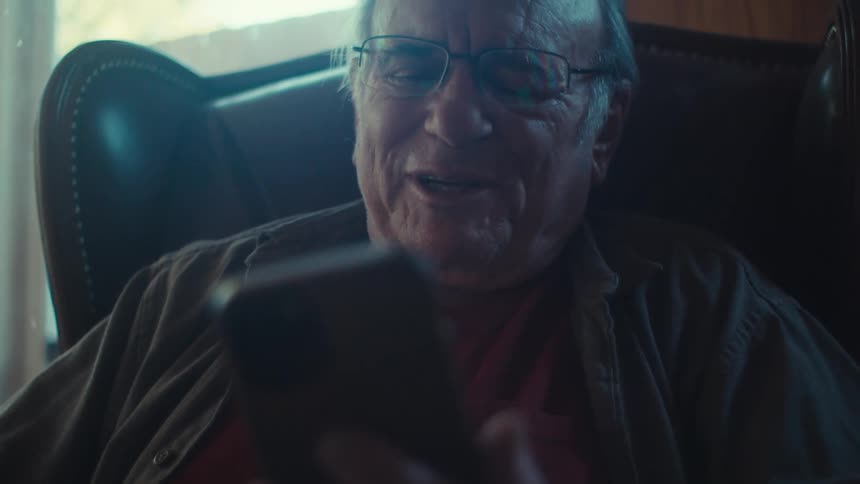 Elderly man smiles while on a video call on his smartphone