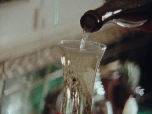 A person pours champagne into three flutes in the kitchen