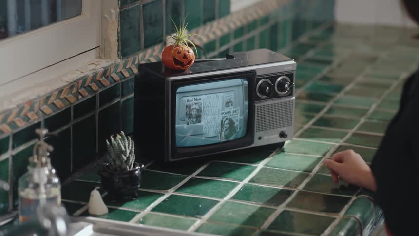 Woman turns off kitchen faucet and watches a small television
